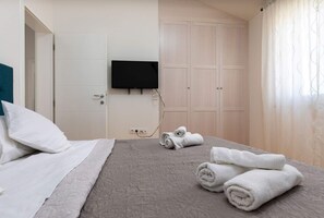 Ett hotellrum med en säng, en tv som är monterad på väggen, en garderob och en uppsättning handdukar på sängen.