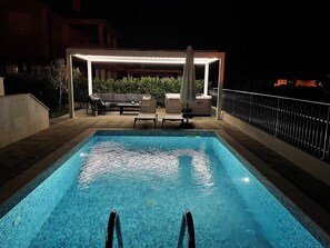 En rektangulär swimmingpool med en kant av kakel, omgiven av en uteplats med utemöbler och en överbyggd sittplats.