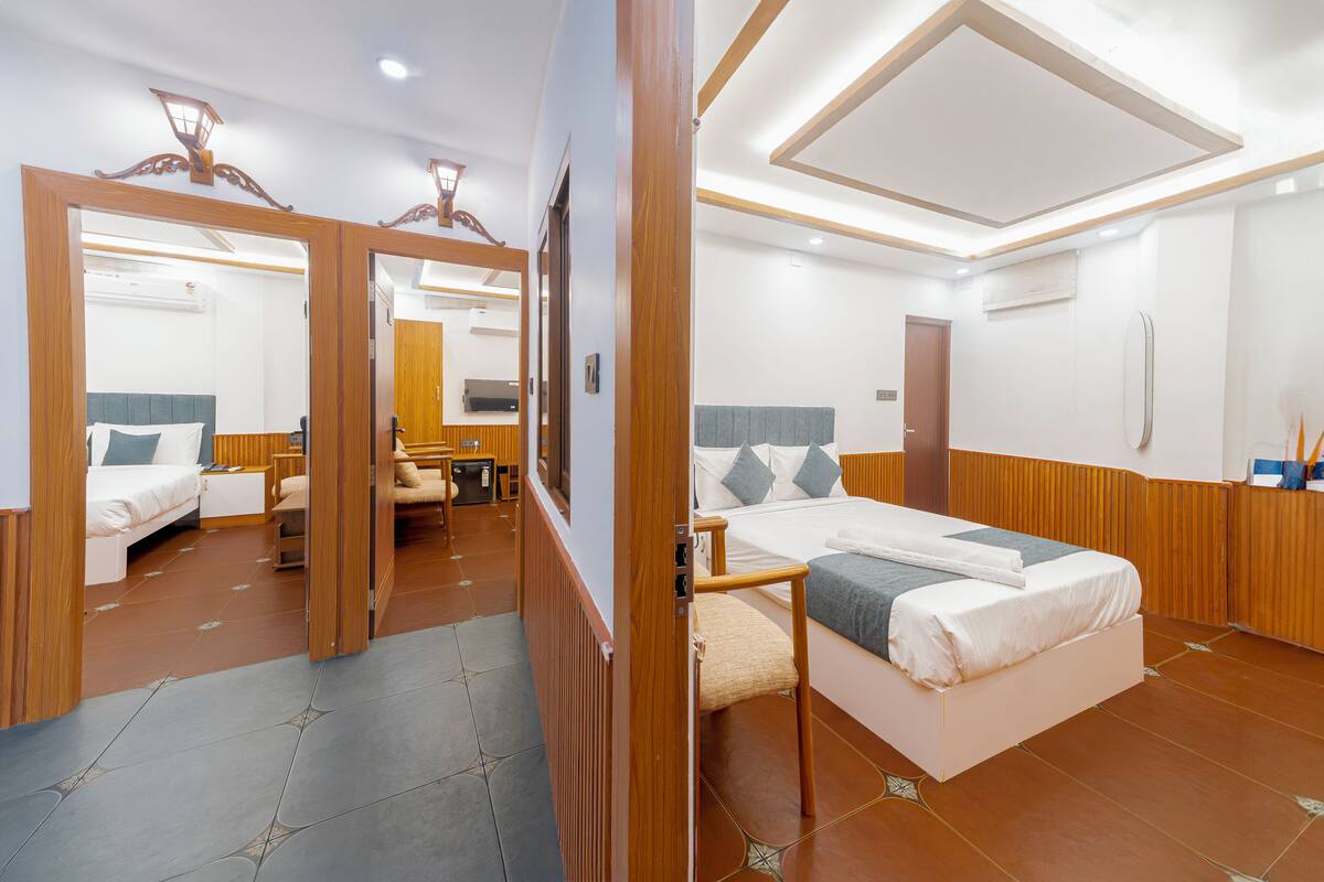 A hotel room with a bed, bedside table, mirror, wardrobe, and a view of another room.
