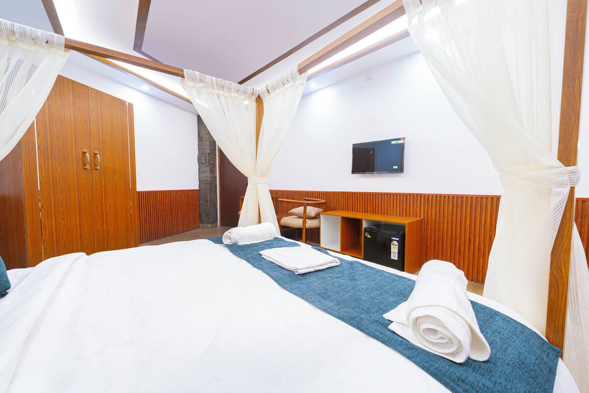 A hotel room with a bed, a desk, a TV, and a minibar.