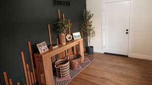 Ein Zimmer mit einer dunklen Wand, einem Holzkonsolentisch mit Körben und einer Topfpflanze, einem gemusterten Teppich und einer weißen Tür.