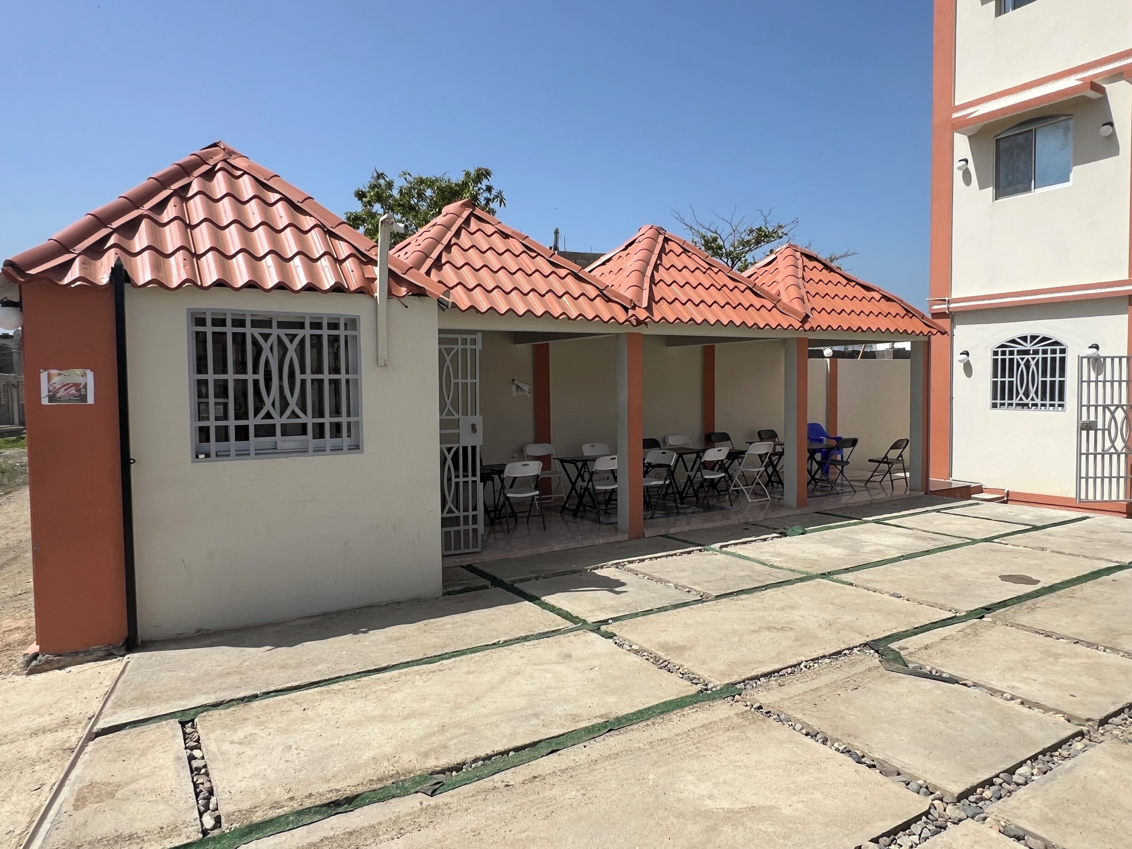 A building with a tiled roof, a covered outdoor seating area with tables and chairs, and a gated entrance.