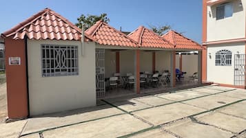 A building with a tiled roof, a covered outdoor seating area with tables and chairs, and a gated entrance.