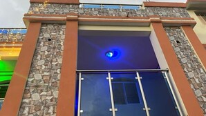 Un bâtiment doté d’une façade en pierre, d’une fenêtre illuminée de couleur bleue et d’une rambarde en métal.