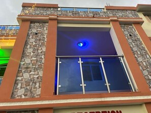 Um edifício com fachada de pedra, uma janela iluminada em azul e um guarda-corrimão de metal.