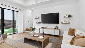 Ett modernt vardagsrum med en platt-TV, en soffa, ett soffbord och en trappa som leder upp till en balkong.