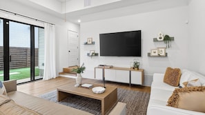 A modern living room with a flat-screen TV, a sofa, a coffee table, and a staircase leading to a balcony.