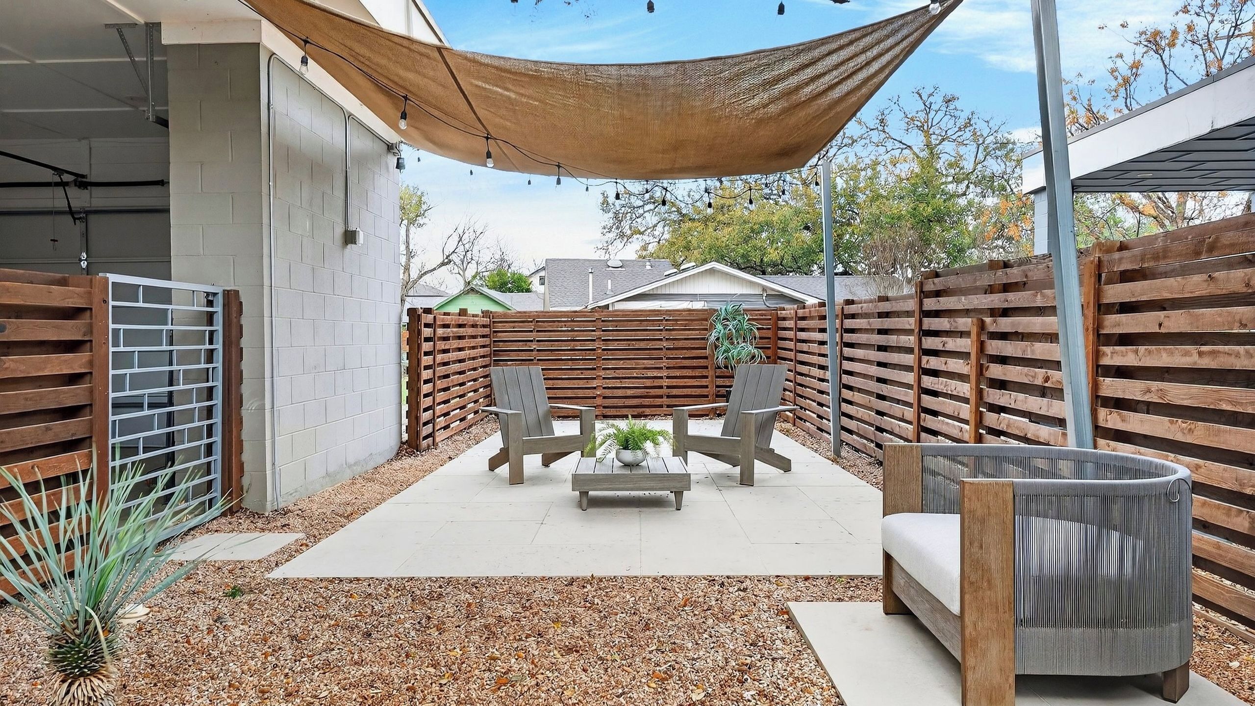 A patio with a table and chairs, a cushioned bench, a woven basket, and a wooden fence.