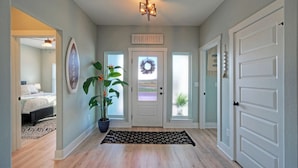 A hallway with a welcome sign, a wreath on the door, and a potted plant. - Mermaid's Oasis by Avantstay Spacious Port A Home + Private Pool + Firepit + Games Near the Beach (Port Aransas)