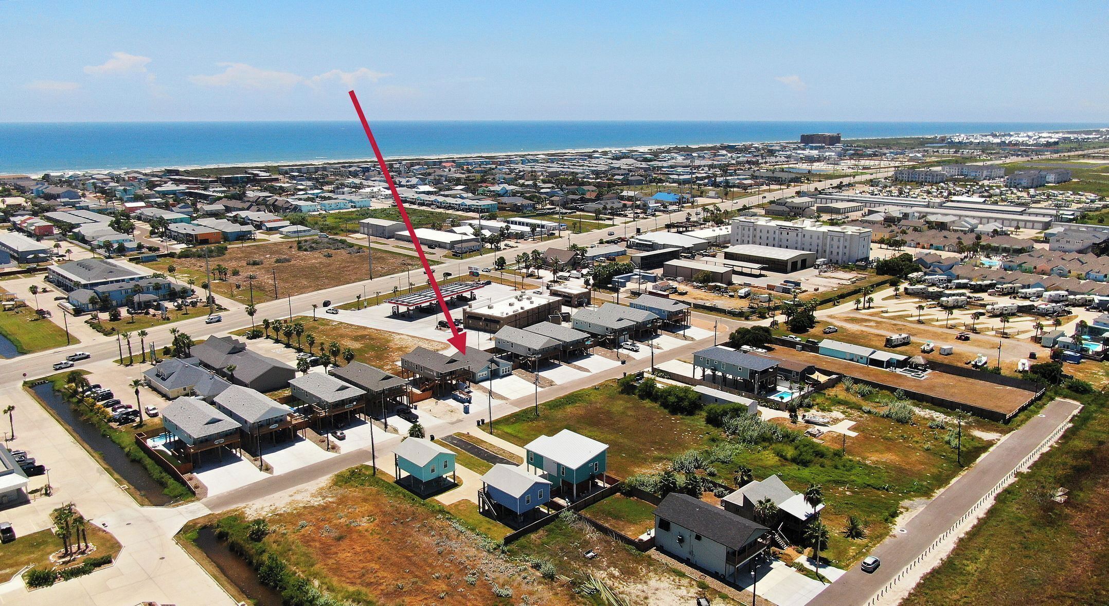 Une vue aérienne d’un quartier résidentiel avec des maisons, des routes et une plage en arrière-plan.