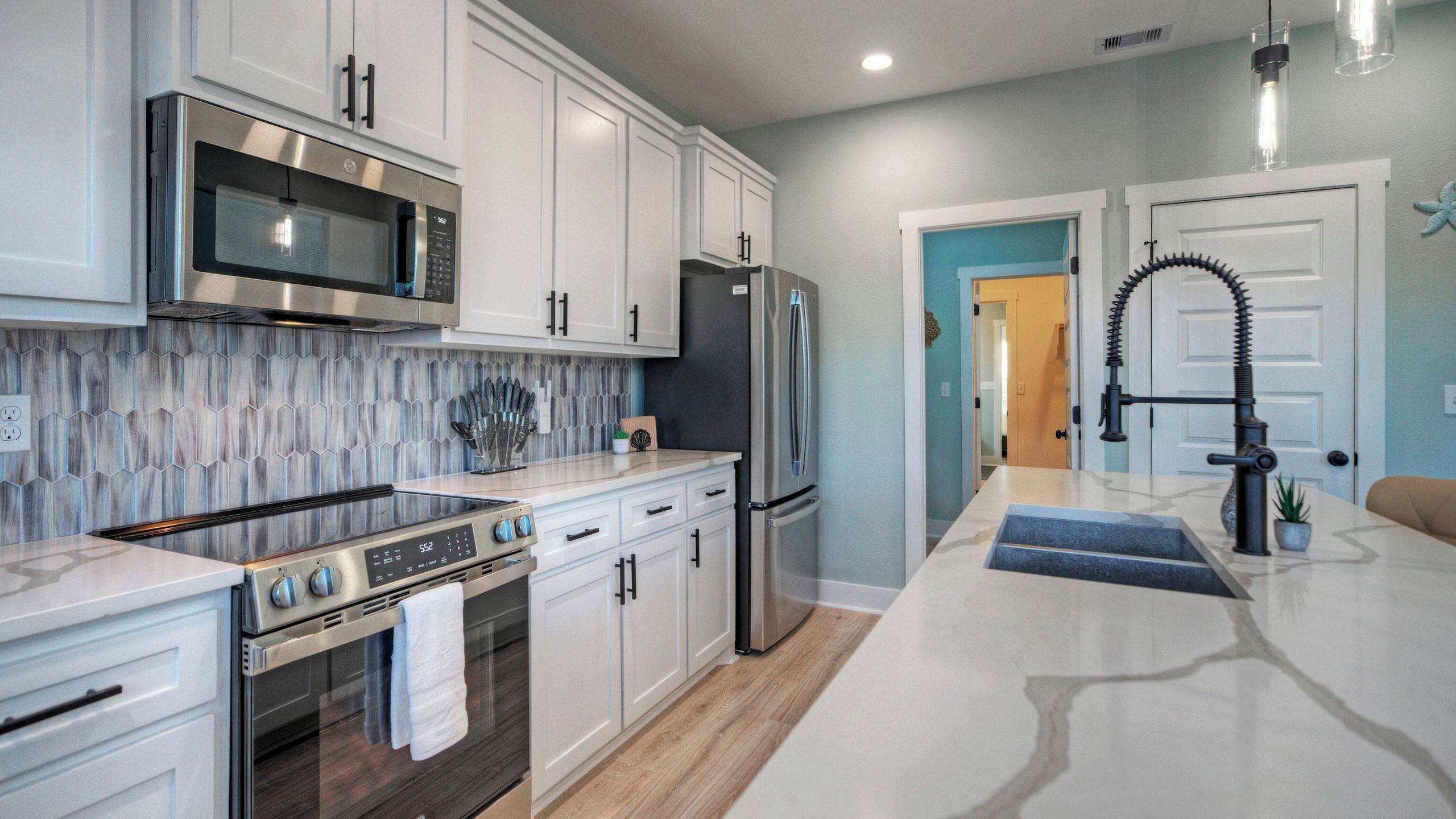 A modern kitchen with stainless steel appliances, white cabinetry, and a wooden backsplash.