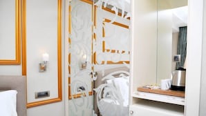 A hotel room with a bed, a bedside table with a lamp, a mirror, and a small kitchenette area.