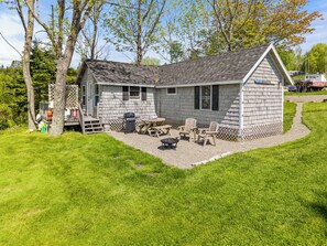 Une petite cabane en bois dotée d’une terrasse, de meubles de jardin et d’un barbecue.