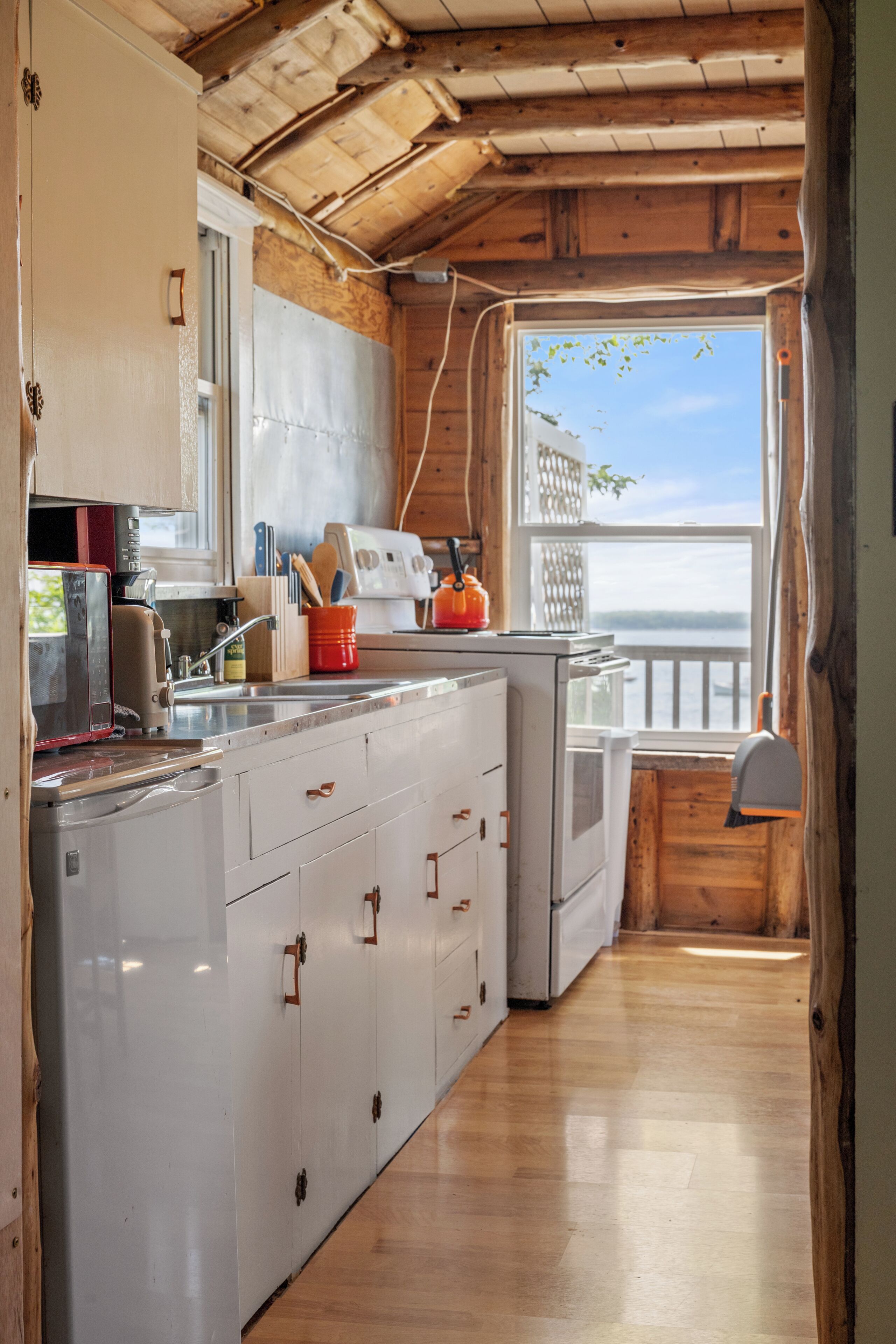 A compact kitchen with wooden cabinets, a built-in oven, and a view of the outdoors through a window.