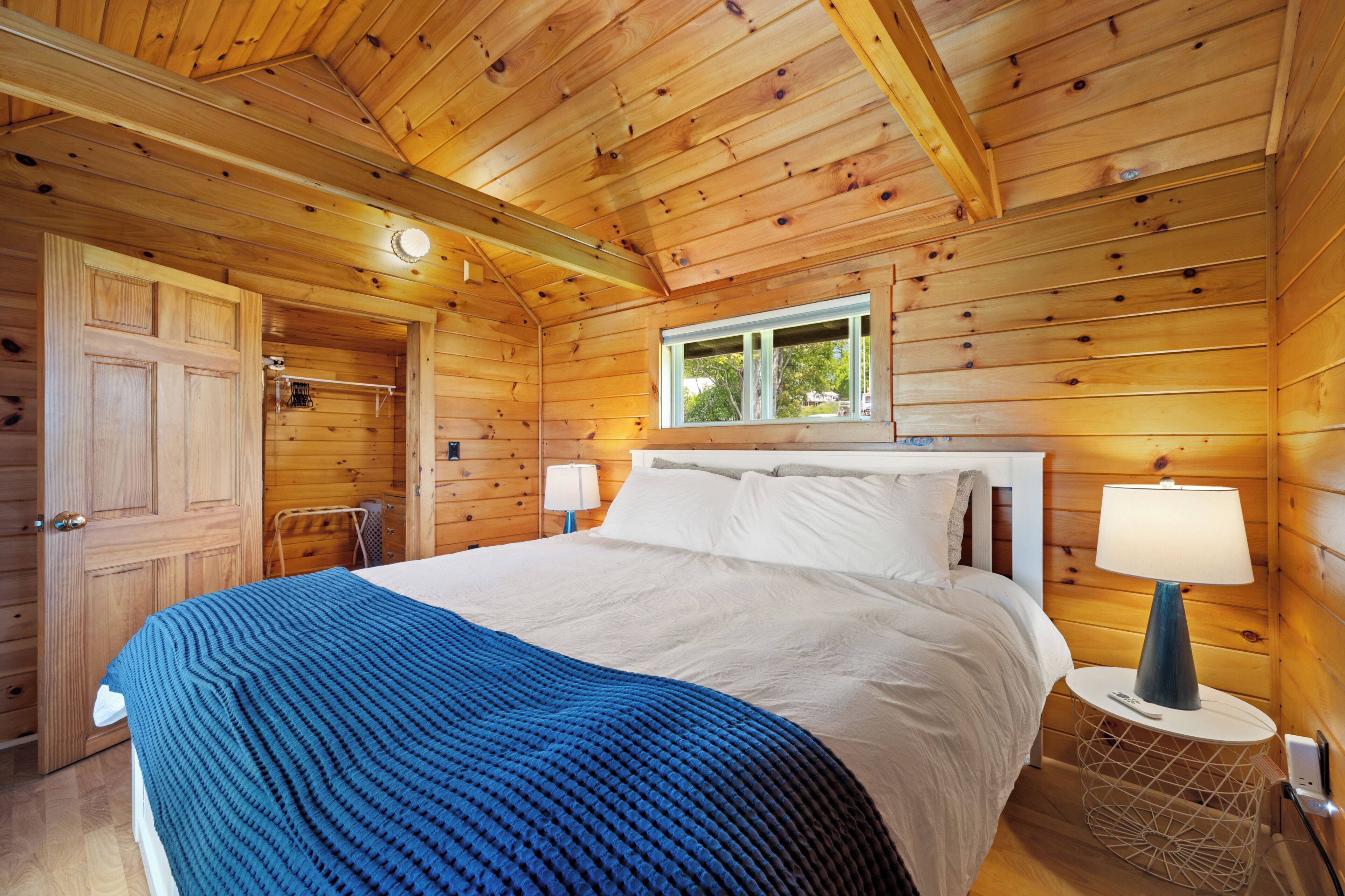 A wooden cabin bedroom with a bed, bedside lamps, and a window.