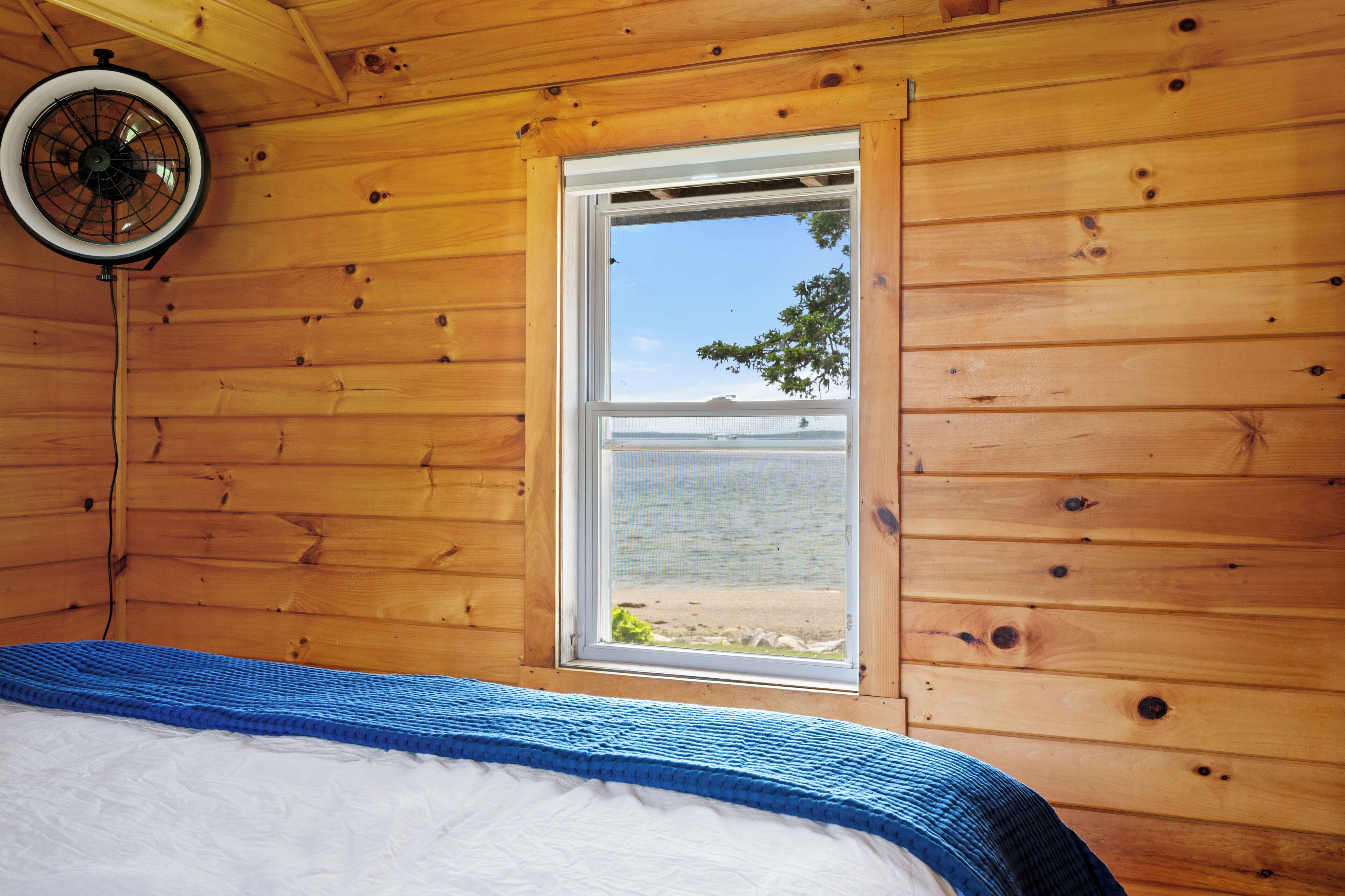 A wooden cabin room with a bed, a window, and a ceiling fan.