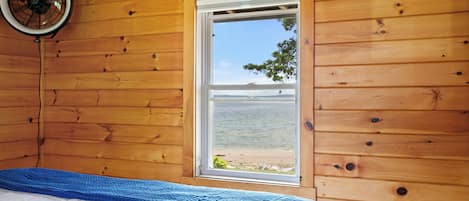 A wooden cabin room with a bed, a window, and a ceiling fan.