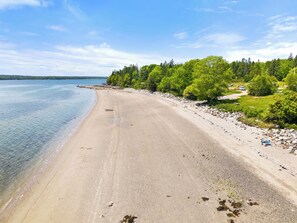 Une plage offrant une vue dégagée sur l’eau, une rive sablonneuse et une zone boisée avec des arbres et des rochers.