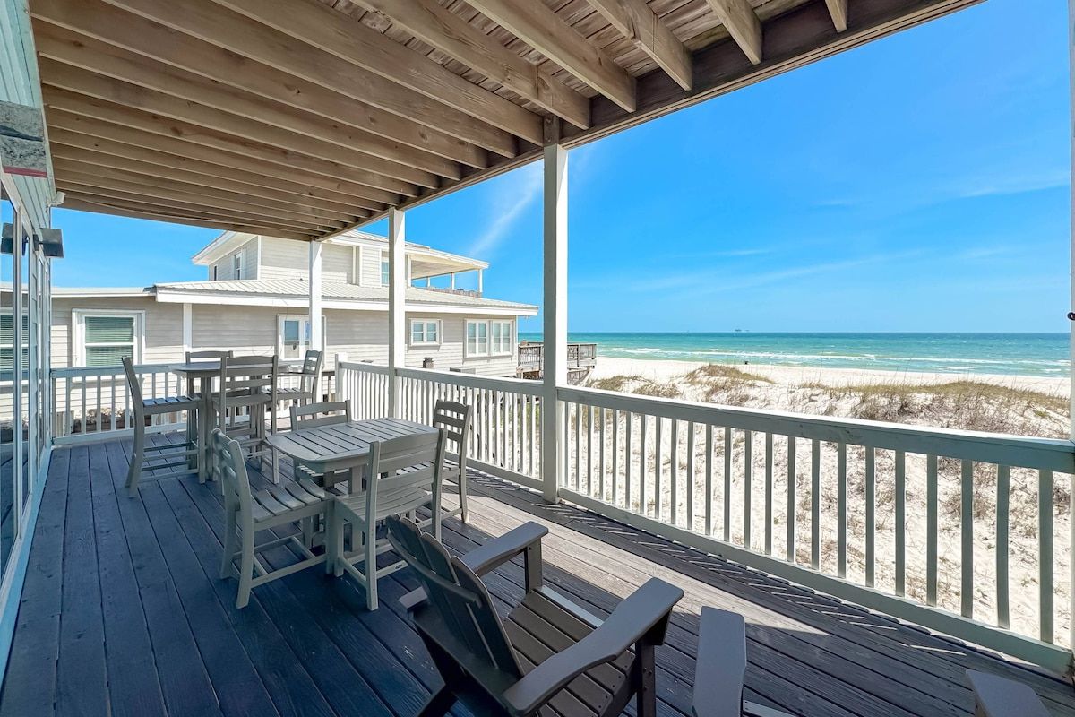 Eine überdachte Terrasse mit Sitzgelegenheiten im Freien, mit Blick auf einen Strand und den Ozean.