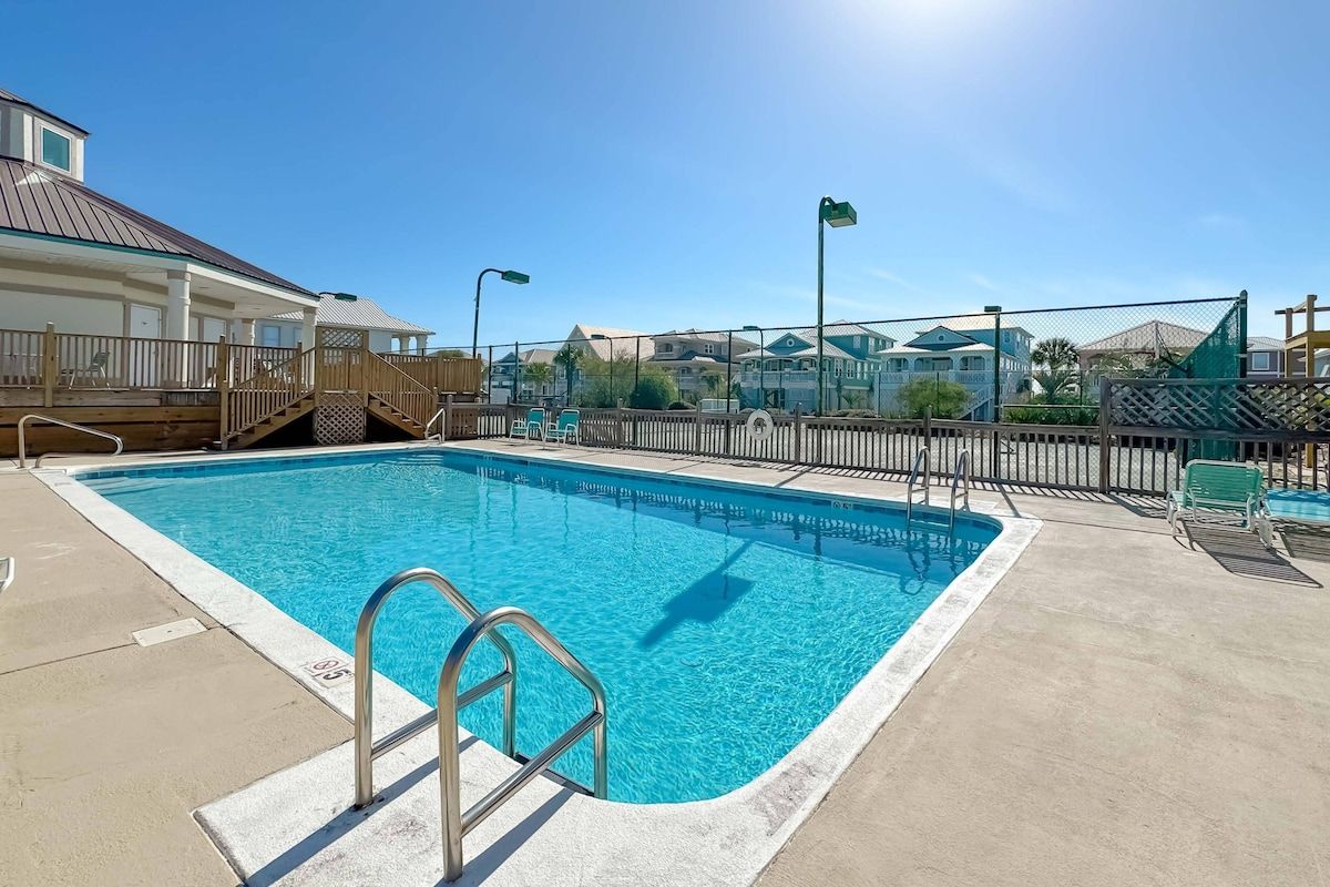 A swimming pool with a metal ladder, surrounded by a fence, and a clear sky.
