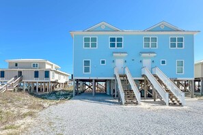 Ein zweistöckiges Strandhaus mit einer Holzterrasse und Treppen, die zum Eingang führen.