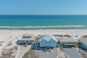 A beachfront property with a central blue house, a covered porch, and a staircase leading to the beach.