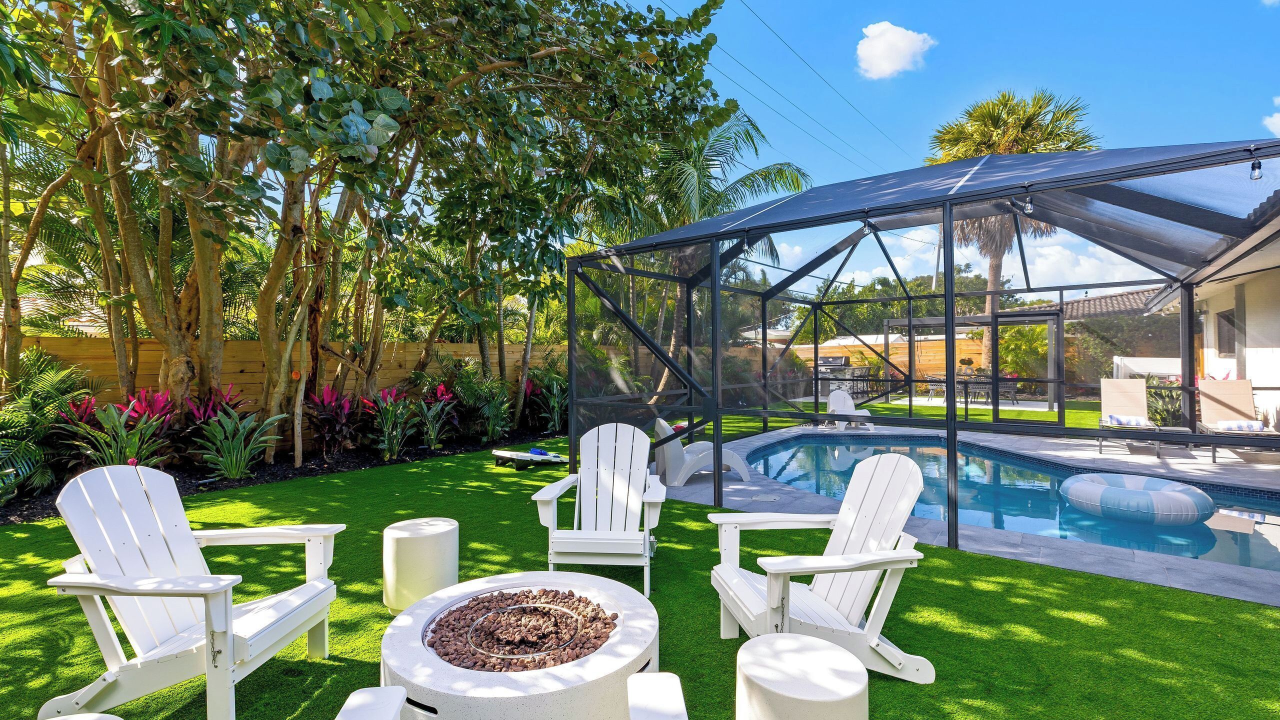 En baghave med pool, hvide stole, bålsted og en overdækket terrasse.