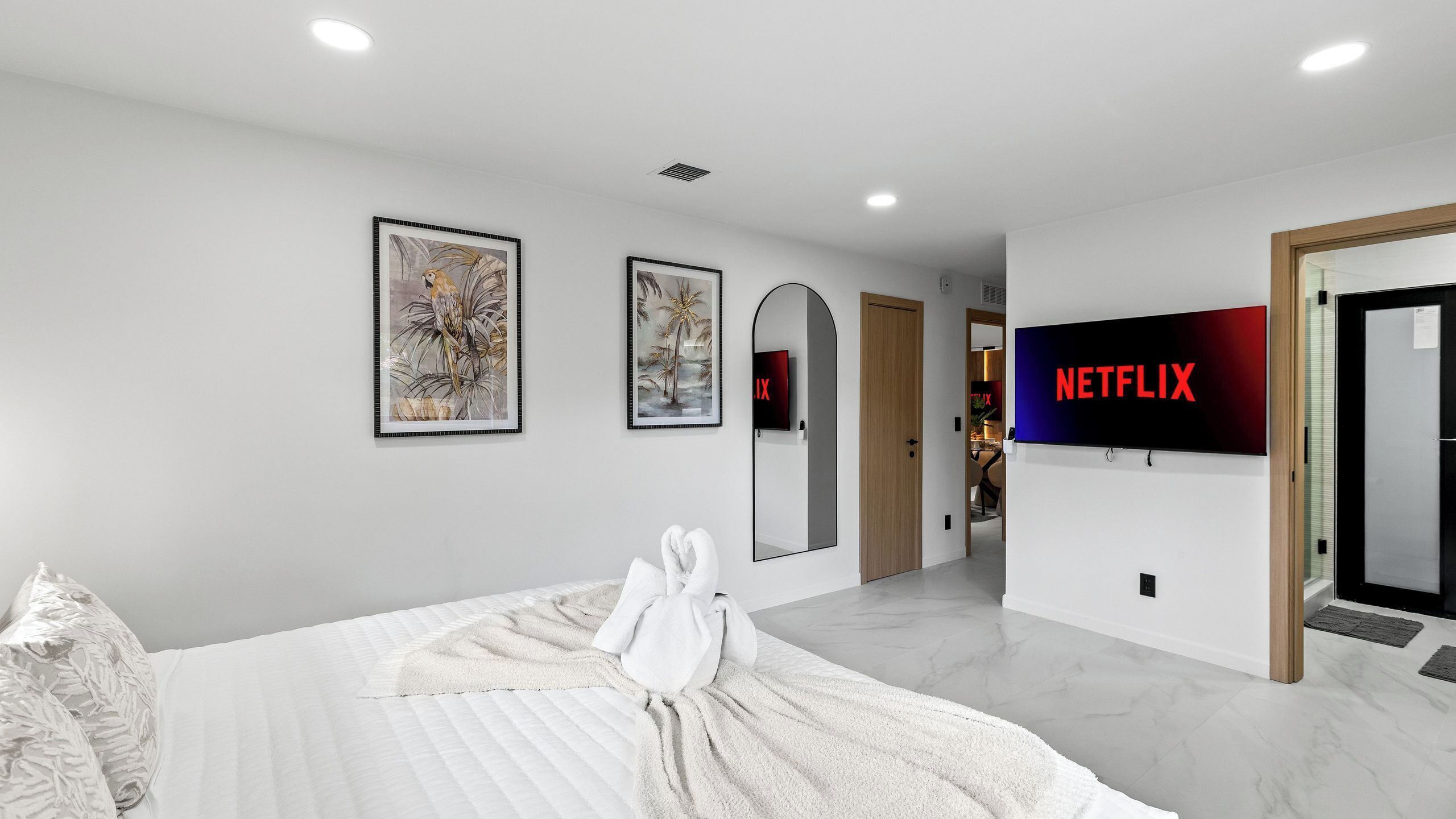 Et moderne hotelværelse med en seng, kunst på væggene, et fjernsyn der viser Netflix-logoet, og en gang der fører til andre værelser.