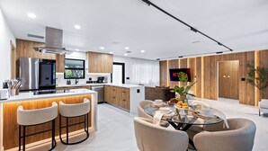 A modern kitchen with a central island, bar stools, and a dining area with a glass table and chairs. - Soleil Oasis by Avantstay Screened Pool + Outdoor Lounge + Firepit Near the Beach (Fort Lauderdale)