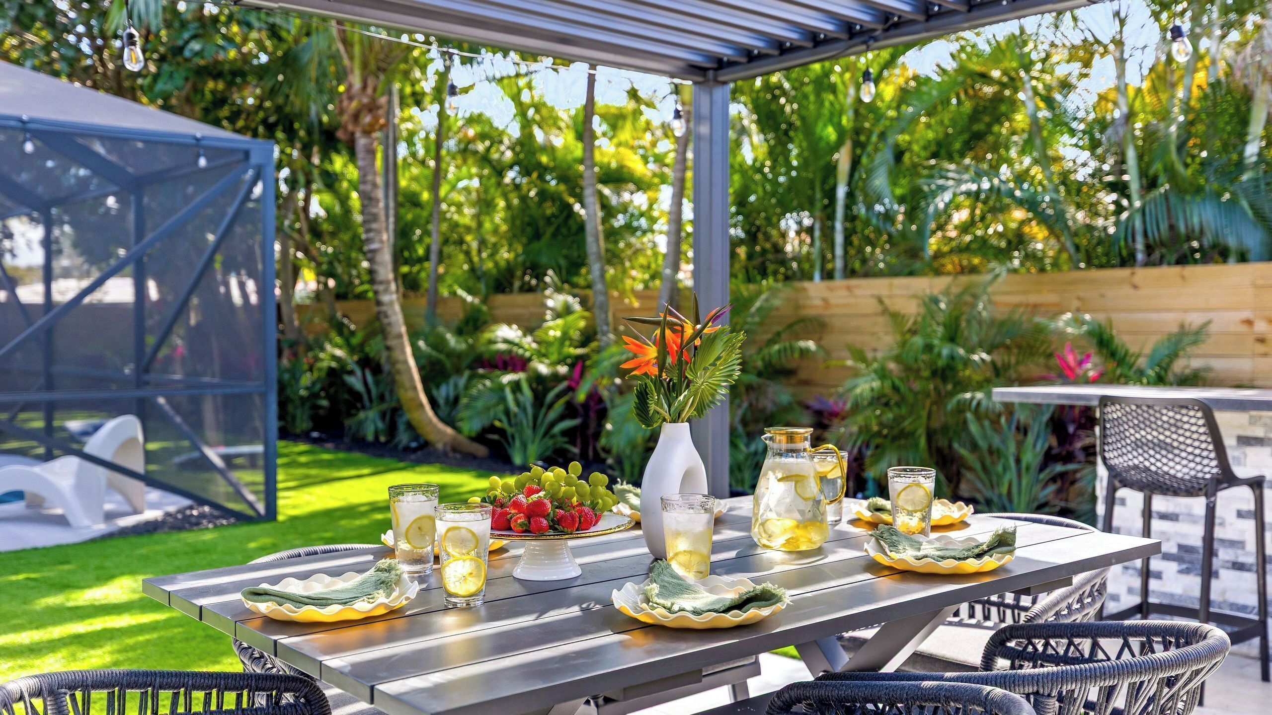 Eine Terrasse im Freien mit Esstisch, umgeben von Pflanzen und einem Holzzaun.