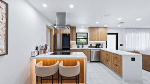 A modern kitchen with a central island, wooden cabinets, stainless steel appliances, and a large window. - Soleil Oasis by Avantstay Screened Pool + Outdoor Lounge + Firepit Near the Beach (Fort Lauderdale)