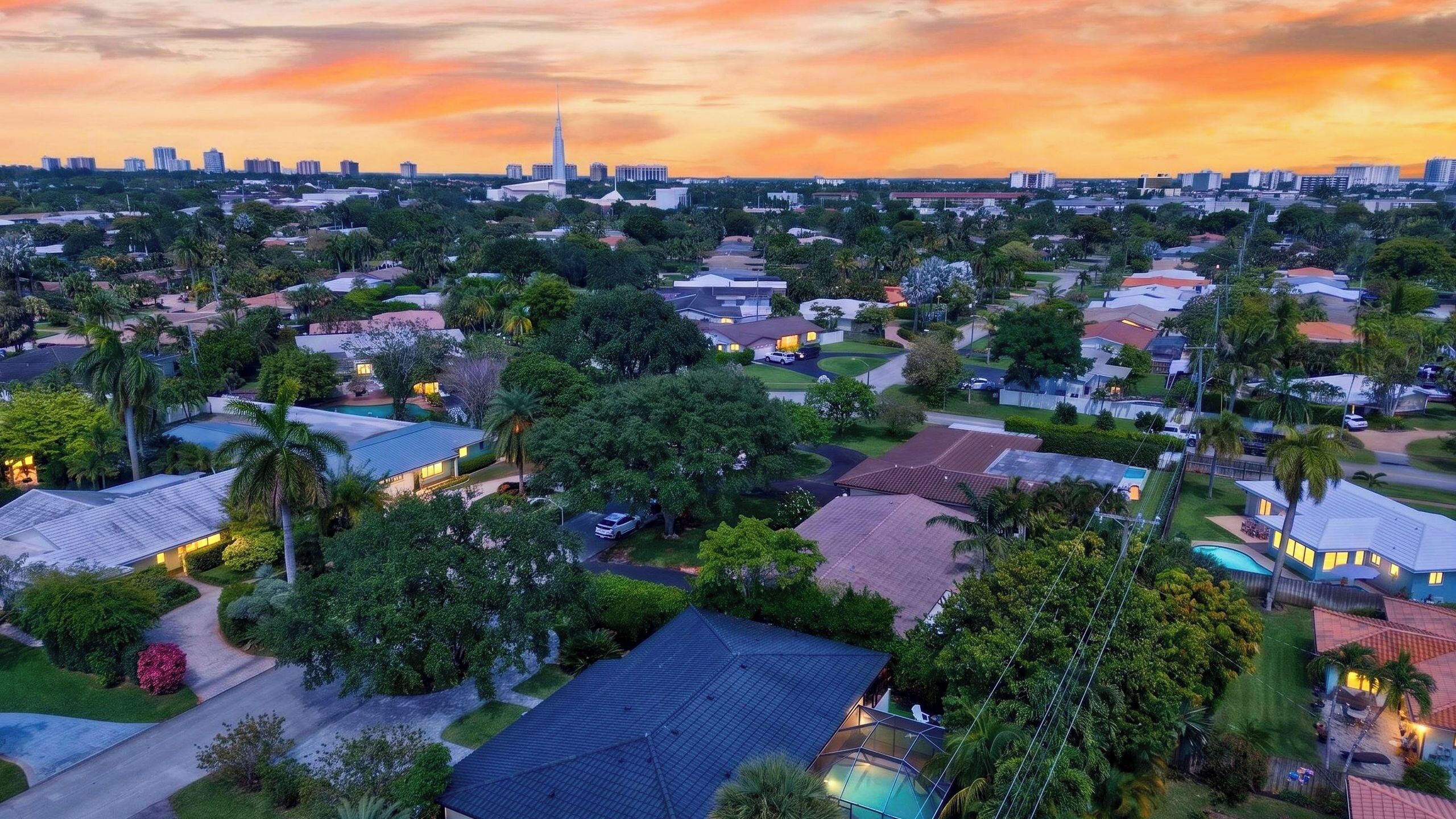 Un quartier résidentiel avec des maisons, des arbres et, au loin, la silhouette d’une ville au coucher du soleil.