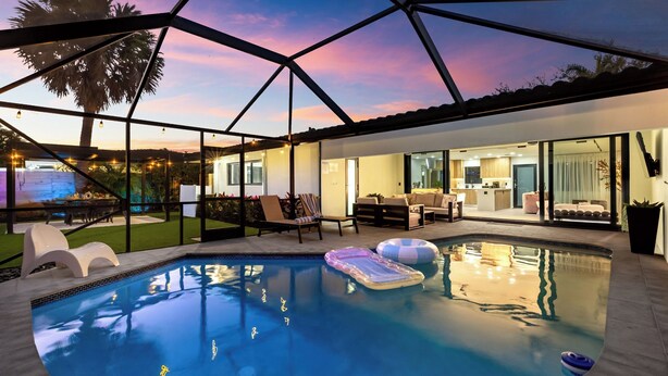 A modern pool area with a glass-enclosed patio, lounge chairs, and a view of the house. - Soleil Oasis by Avantstay Screened Pool + Outdoor Lounge + Firepit Near the Beach (Fort Lauderdale)