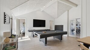 Amplia habitación con mesa de billar, televisor montado en la pared y puerta que da a otra zona.