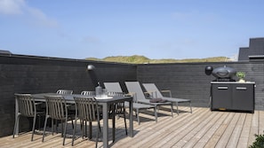 Een terras buiten met een eettafel, stoelen en een barbecue.
