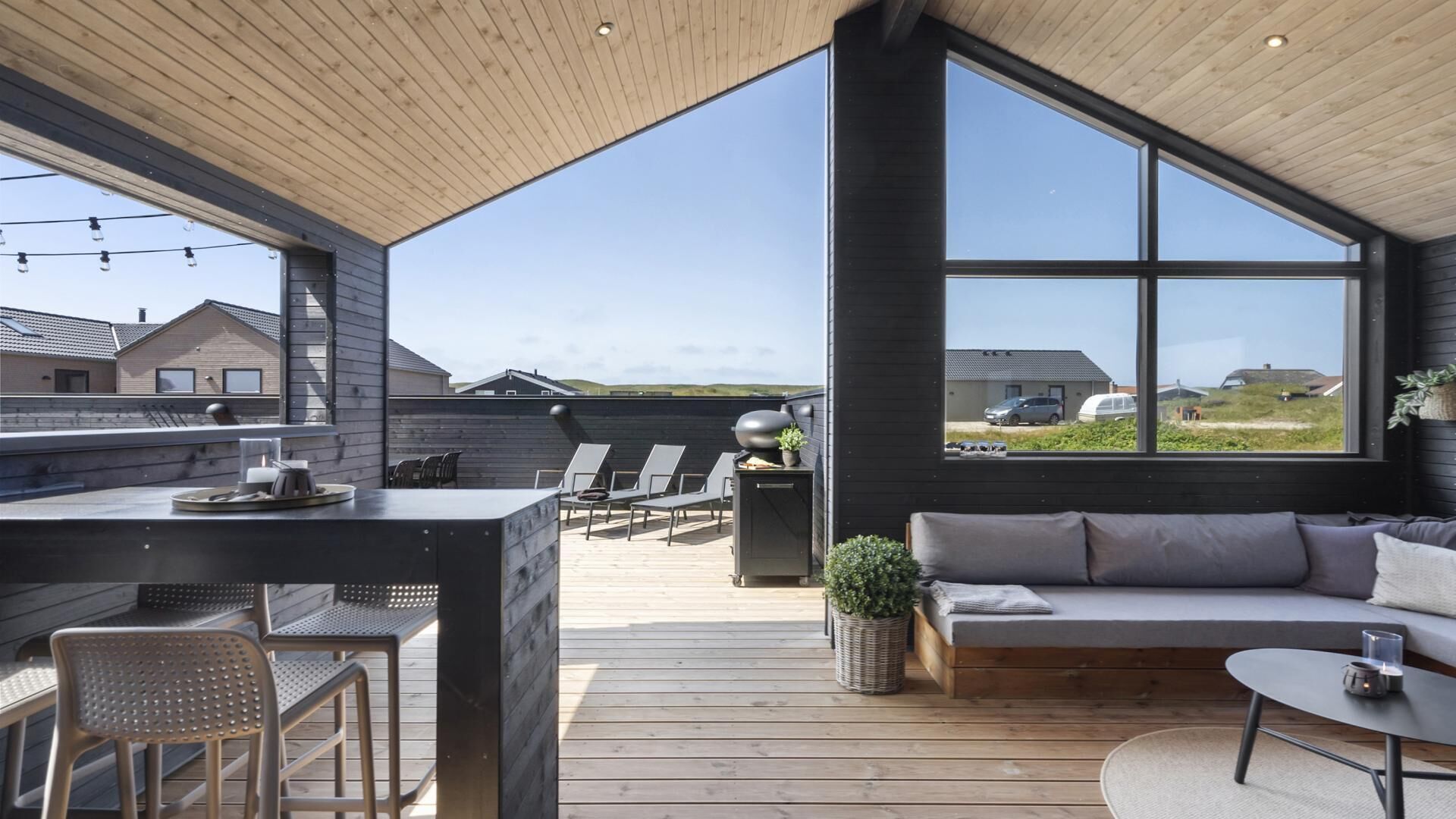 A modern outdoor living space with a wooden deck, seating area, and a large window offering a view of the surrounding landscape.