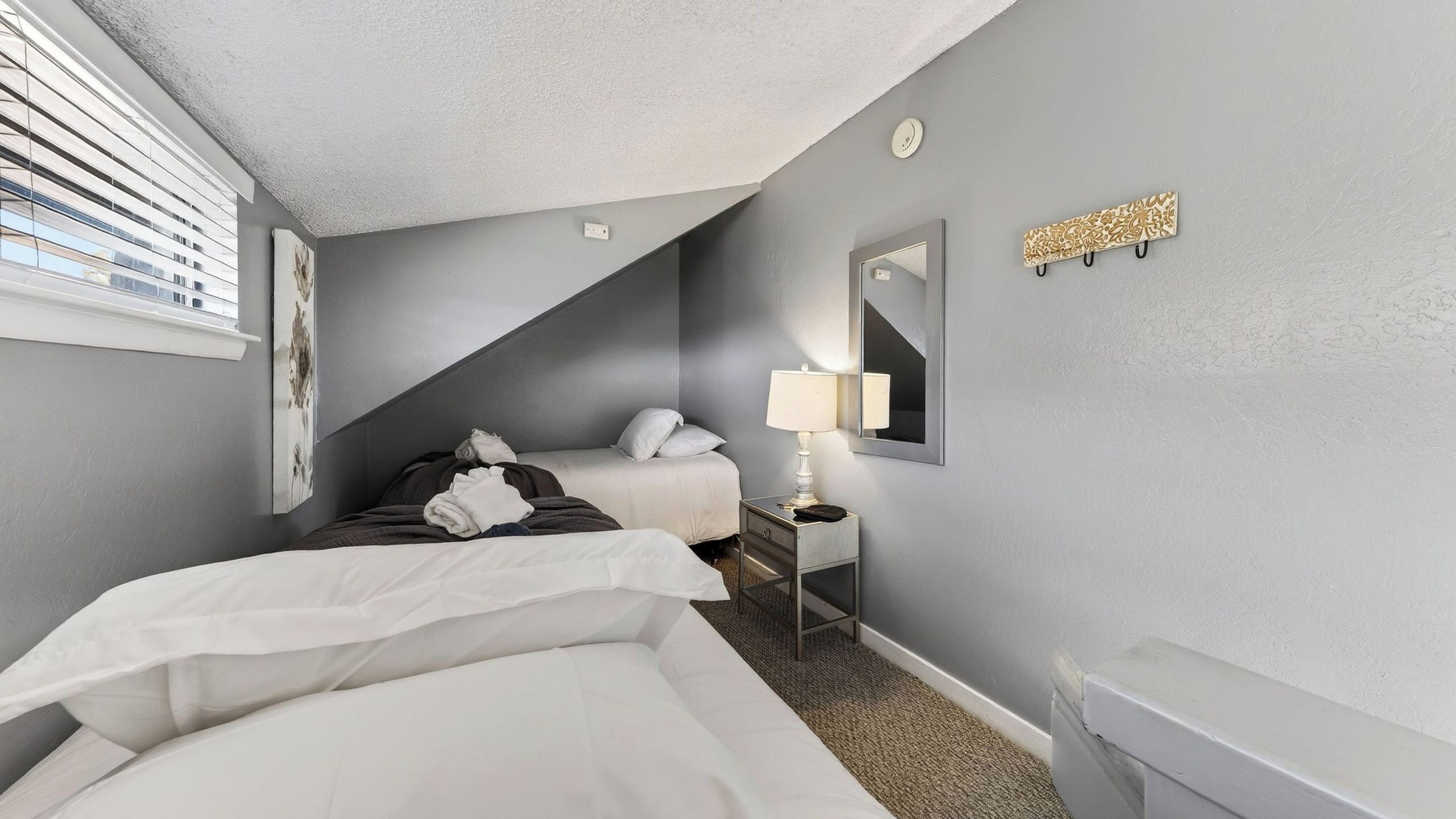 A bedroom with two beds, a bedside table with a lamp, a mirror, and a decorative wall piece.