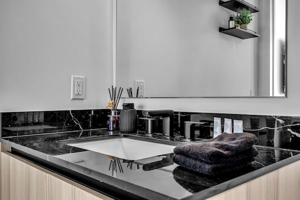 Una cocina moderna con encimera de mármol negro, un lavamanos de acero inoxidable y un perchero para toallas.