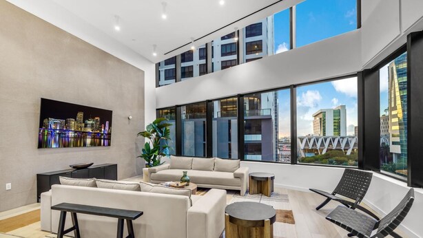 Een ruime woonkamer met een hoge plafond, grote ramen met uitzicht op de stad, een moderne zithoek, een salontafel en een minimalistische fauteuil.