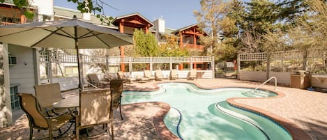 A backyard with a swimming pool, patio furniture, and a covered seating area.