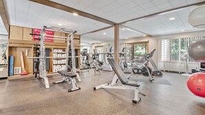 A gym with various exercise equipment, wooden beams on the ceiling, and large windows. - Two Pools Tennis Balcony Hiking Golf Biking Restaurants Activities Summer Perfection! (Park City)
