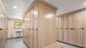 A locker room with wooden lockers, a bench, and a window with a view of greenery. - Two Pools Tennis Balcony Hiking Golf Biking Restaurants Activities Summer Perfection! (Park City)
