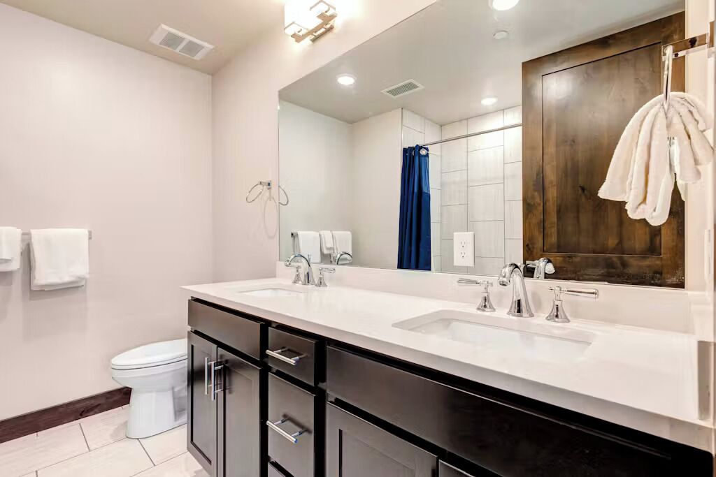 Un baño moderno con lavamanos doble, un espejo grande y cortina de ducha.