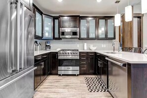 A modern kitchen with stainless steel appliances, dark cabinetry, and a herringbone-patterned rug. - Blackstone Luxury 2br, Walk to Skiing at Cabriolet, Mountain View, Shared Pool and Hot tub, Gym (Park City)