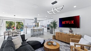 A modern living room with a black sofa, a coffee table, and a TV displaying 'NETFLIX'. - Soleil Breeze by Avantstay Pool + Canalfront Home + Outdoor Dining Canal Deck + Kayak 10 Mins to the Beach (Fort Lauderdale)