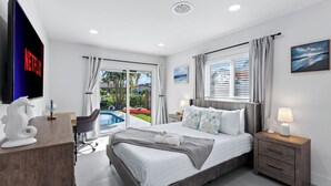 A modern hotel room with a bed, a desk, a chair, a TV, and a view of the outside. - Soleil Breeze by Avantstay Pool + Canalfront Home + Outdoor Dining Canal Deck + Kayak 10 Mins to the Beach (Fort Lauderdale)