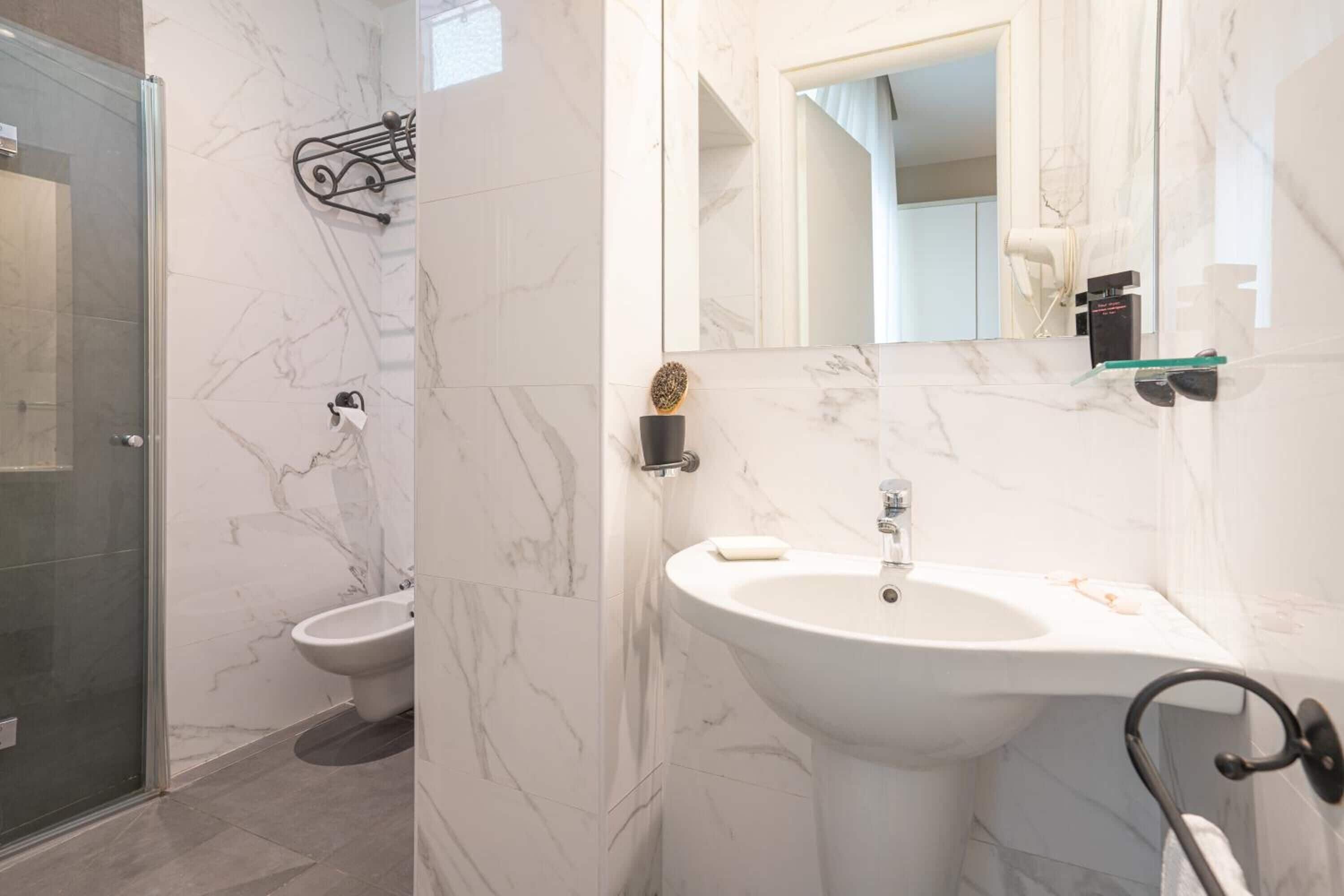 Une salle de bain avec une douche à parois de verre, un lavabo sur colonne blanc, un miroir et un porte-serviettes.