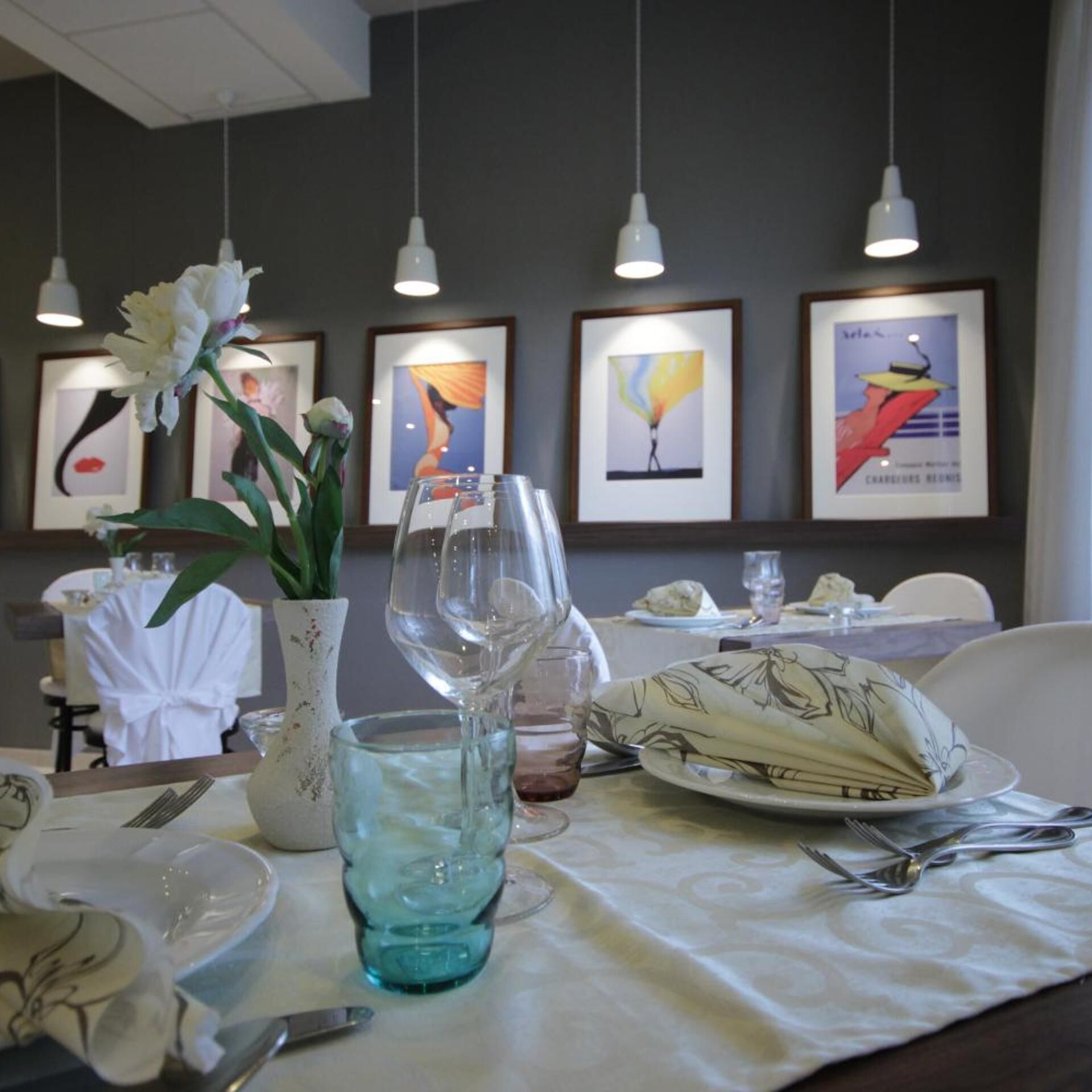 A dining table set with plates, glasses, and cutlery, with framed artwork on the wall.