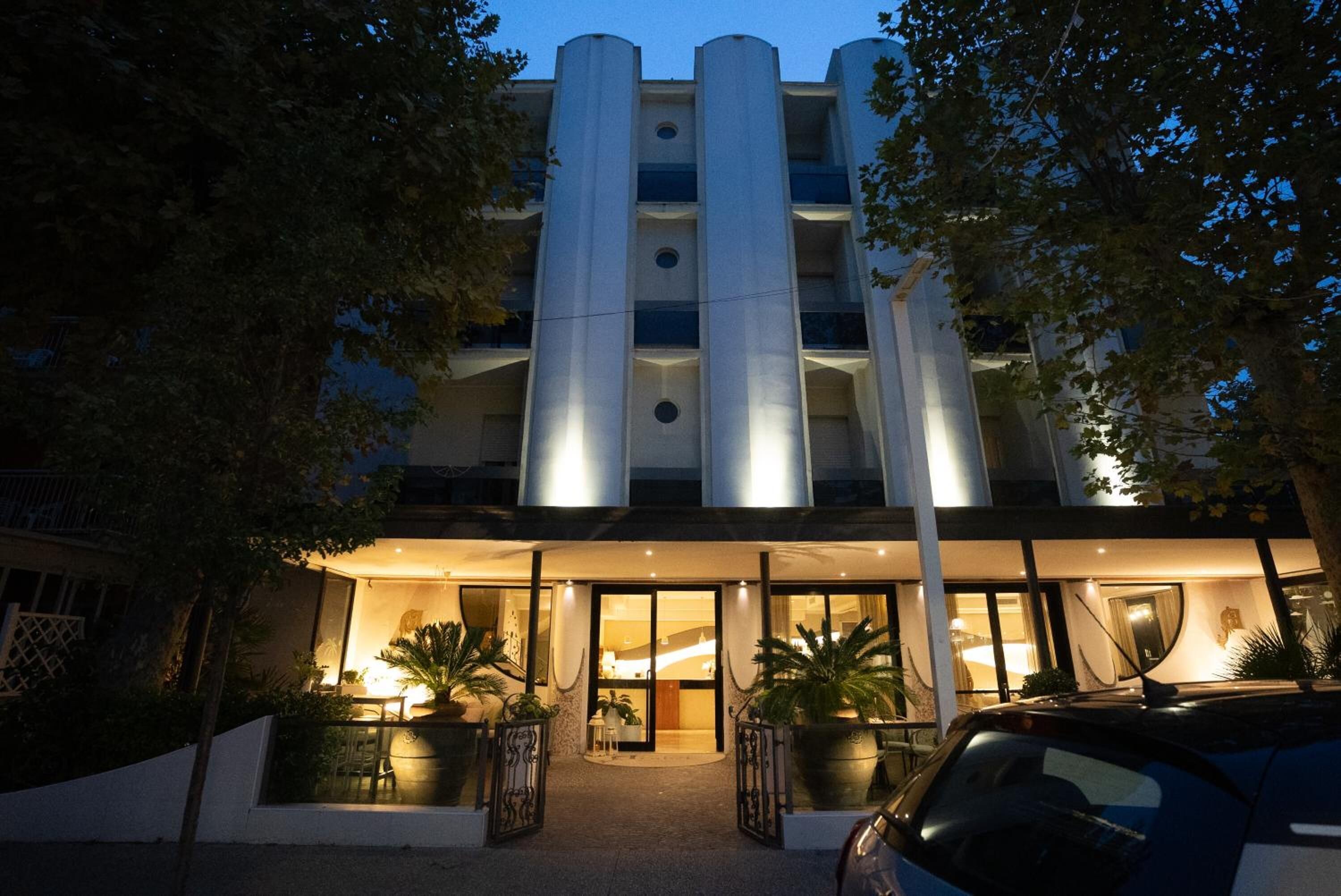 A modern hotel with a central entrance, large windows, and a parking area.