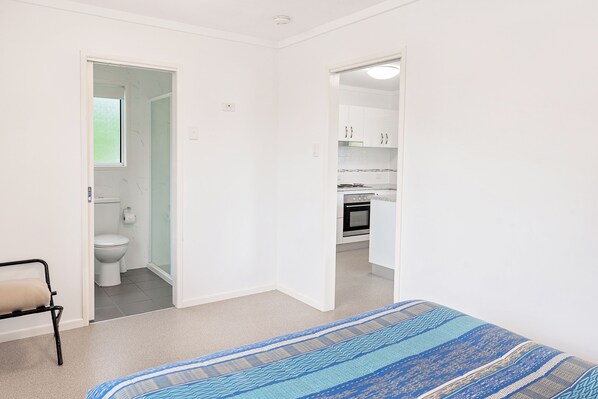 Une chambre avec un lit, une salle de bain avec des toilettes et une cuisine équipée d’armoires et d’appareils électroménagers.